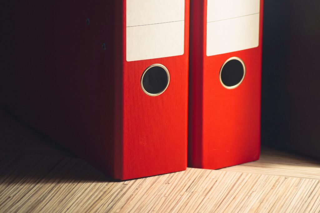 Home Close-up of two red lever arch files on a wooden desk in a modern office setting.